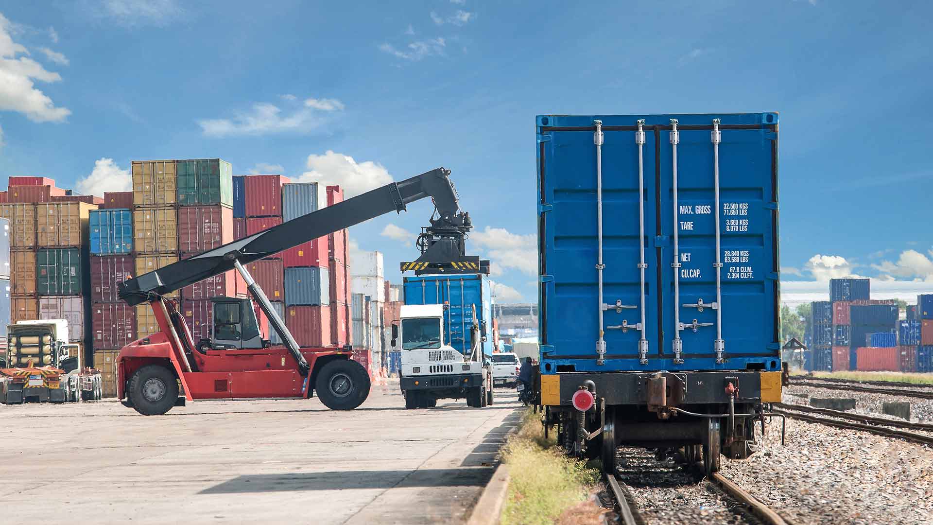 Cargo containers being moved from freight truck to freight train for transport at port